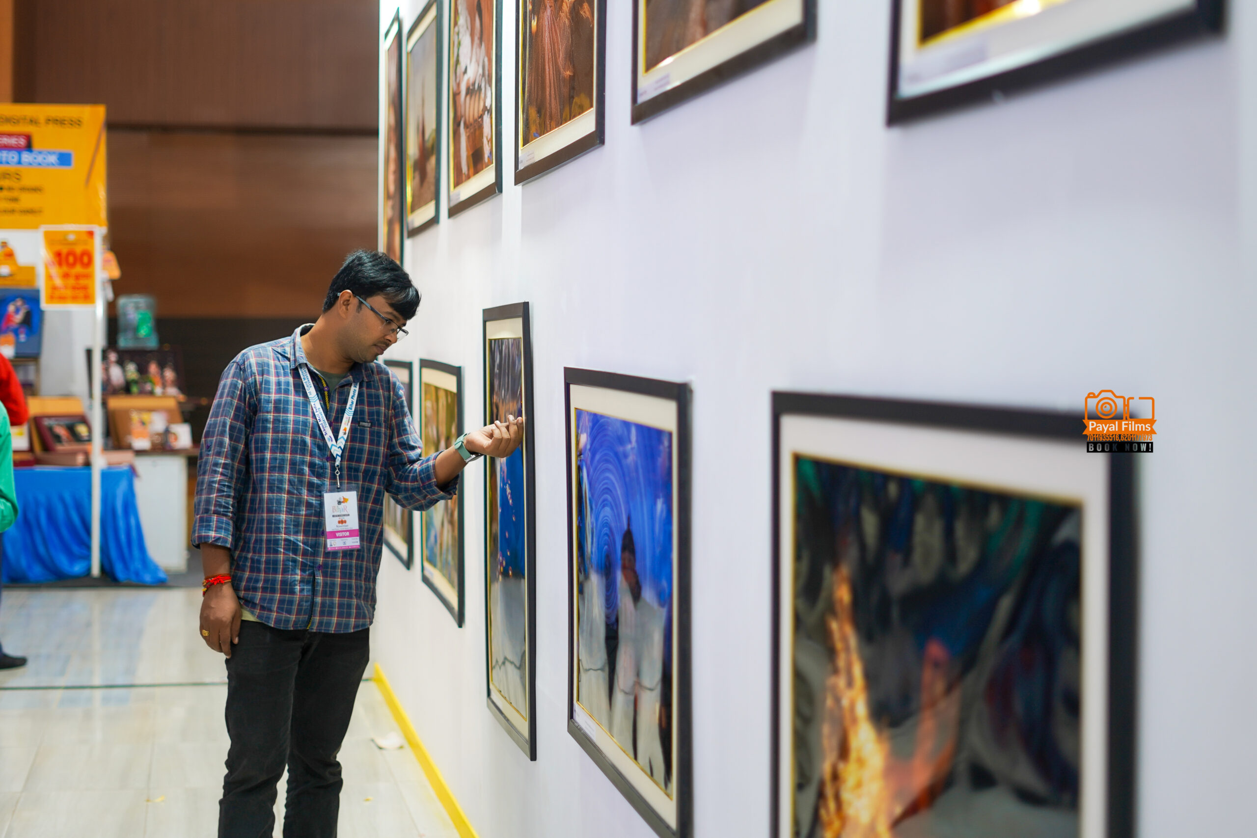 Payal Films cinematic wedding photographer viewing framed wedding photos at gallery exhibition in Bihar, wearing event badge