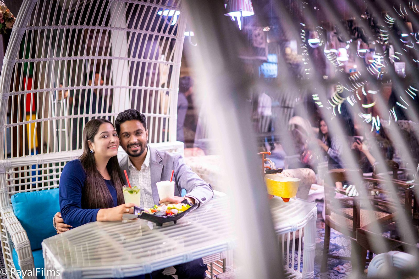 A happy couple on a cafe date holding drinks, captured by Payal Films in a cinematic style.