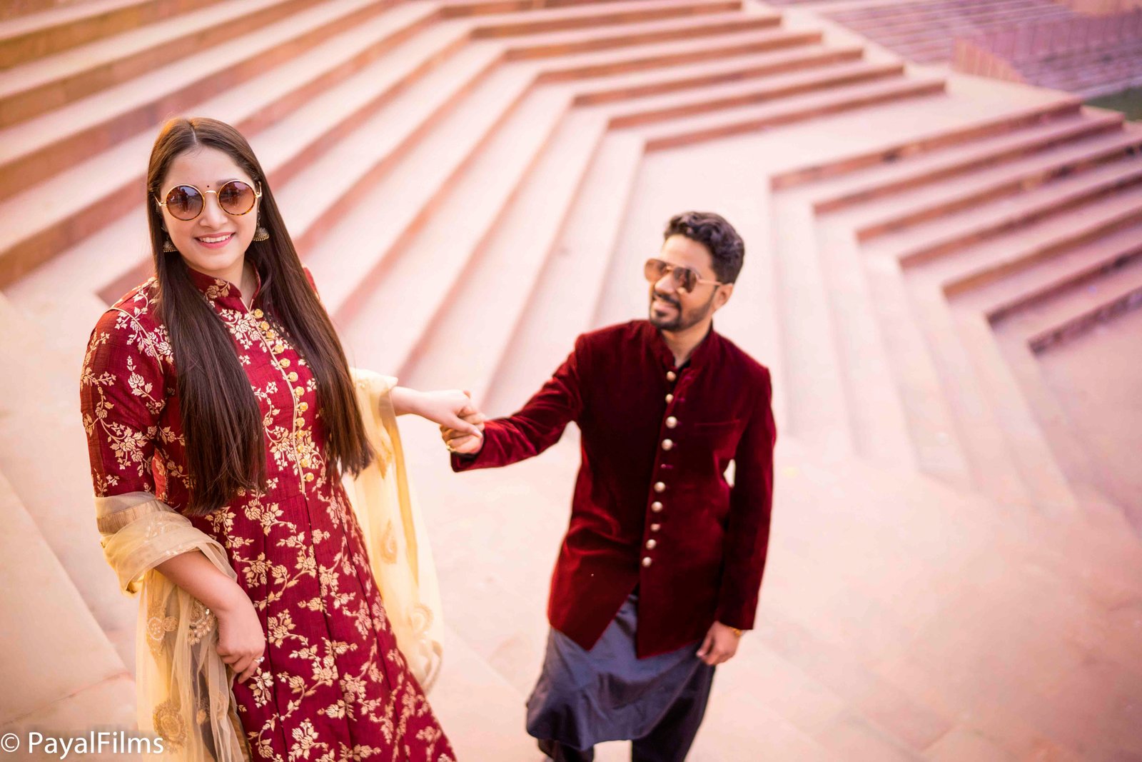 A couple smiling while woman touches man's cheek in front of a red historical monument by Payal Films