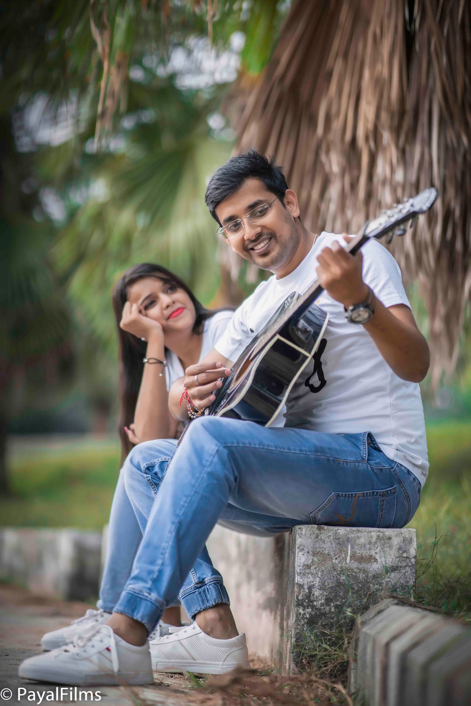 A man playing guitar for his smiling partner during a romantic outdoor pre-wedding shoot by Payal Films in Khagaria.