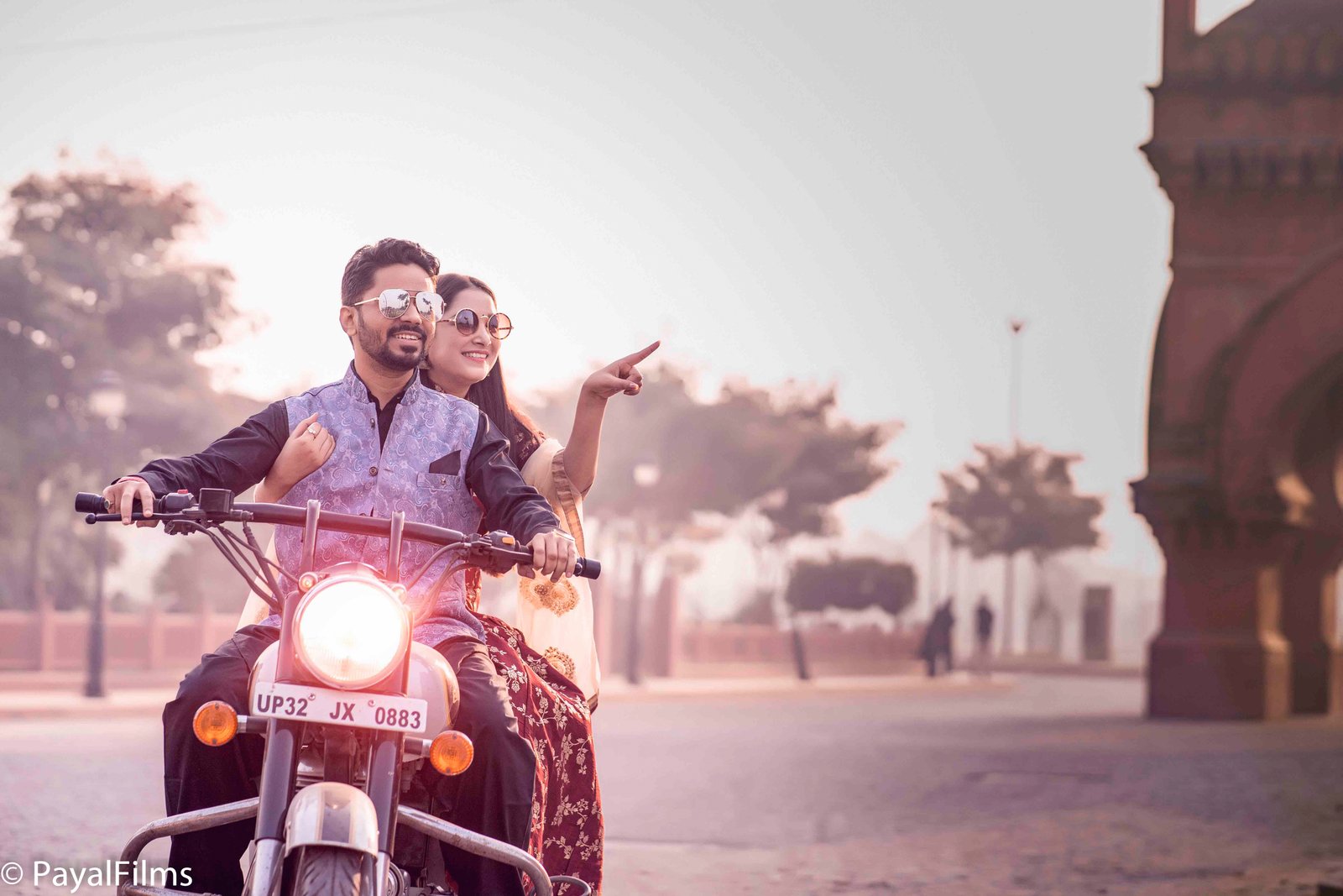 Stylish couple posing with a Royal Enfield bike at a red fort, captured by Payal Films in Khagaria.