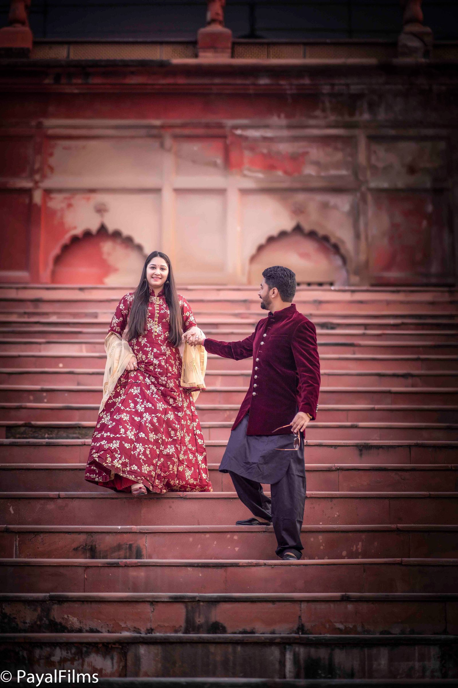Royal couple pre-wedding portrait walking on red stone heritage stairs by Payal Films Bihar