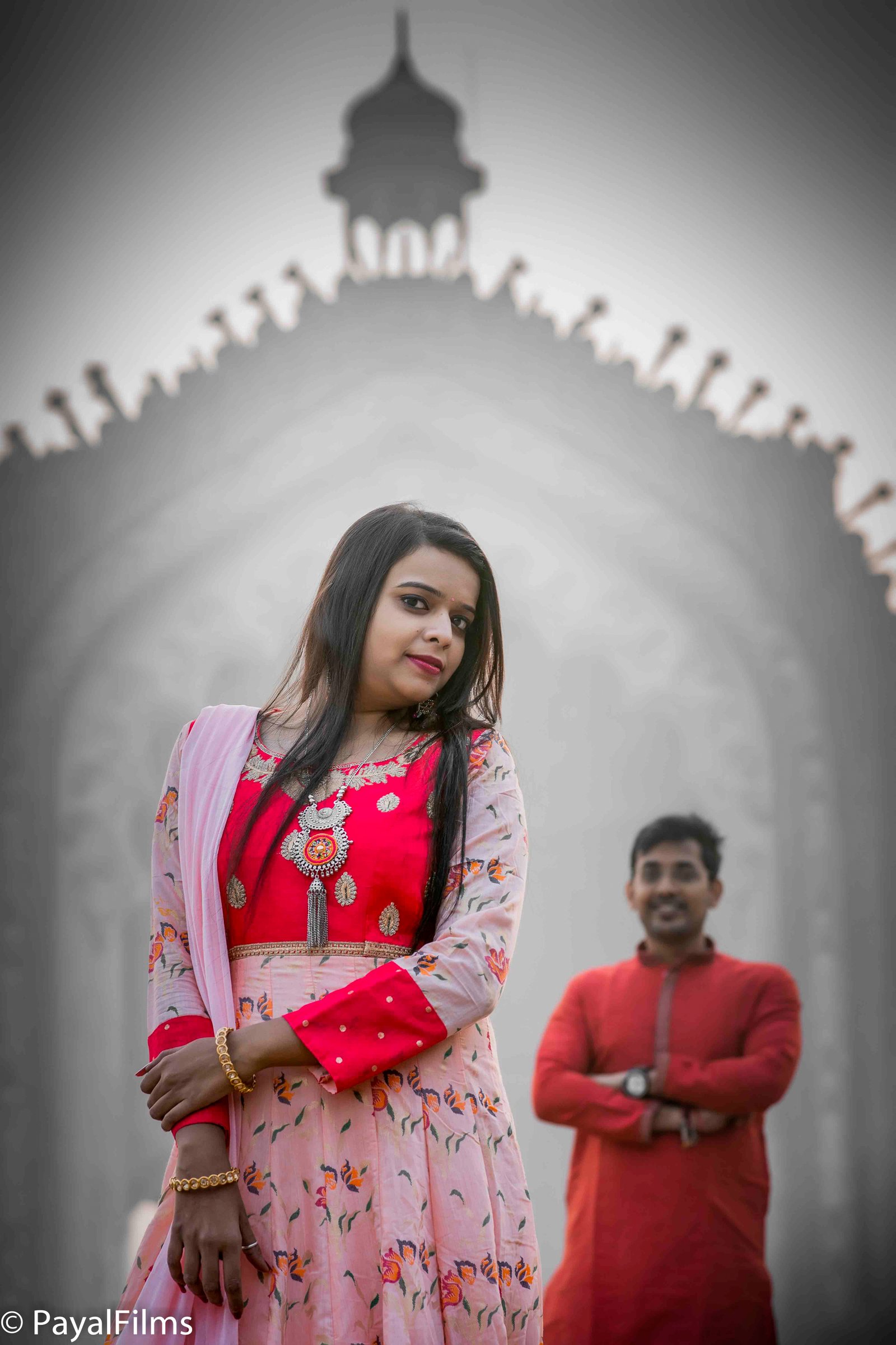 Indian bride in red and pink anarkali dress with groom in background by Payal Films in Khagaria