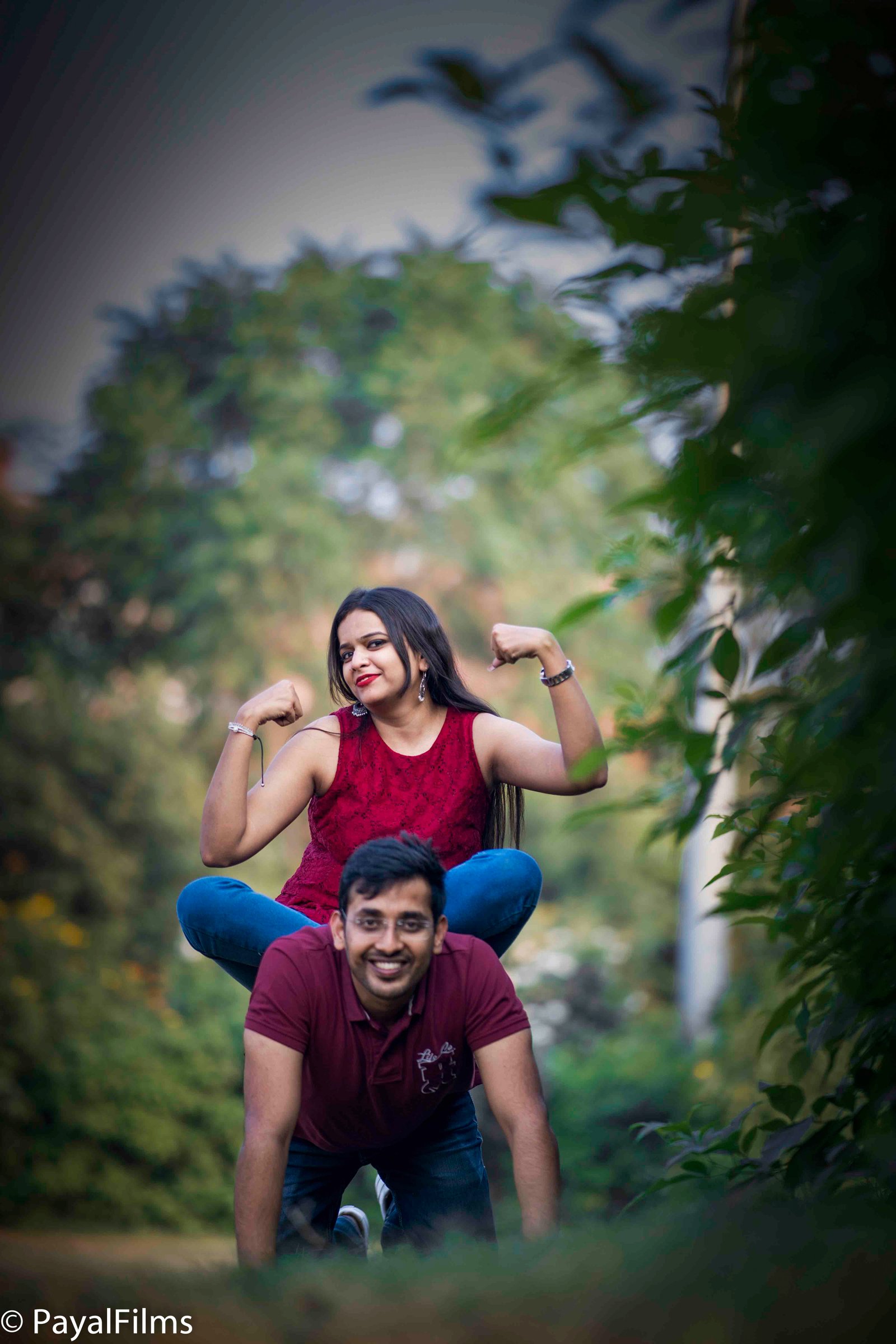 Playful pre-wedding couple pose with woman flexing muscles on man's back by Payal Films in Khagaria.