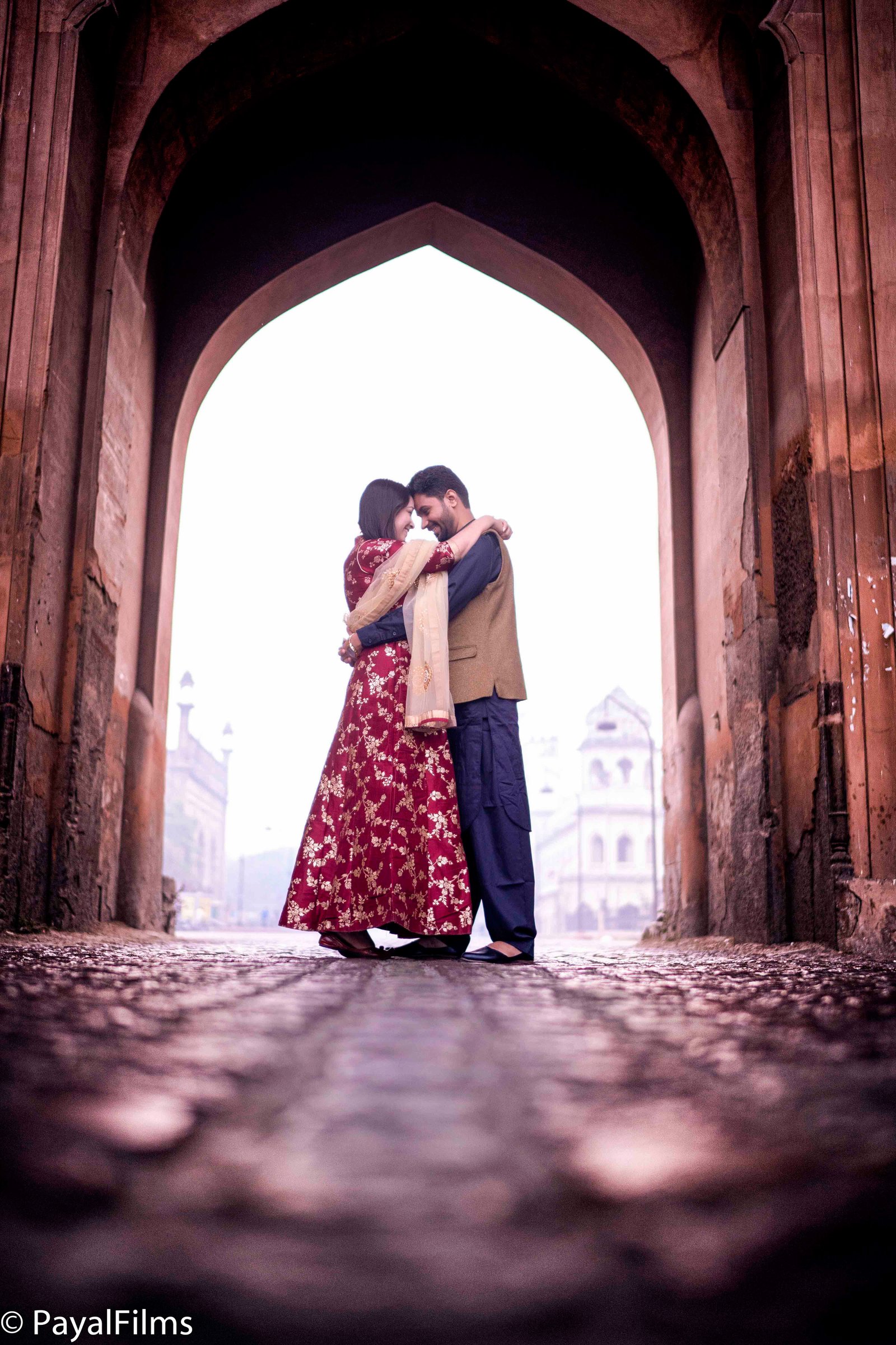 Romantic couple hugging under archway maroon anarkali ethnic attire by Payal Films Bihar
