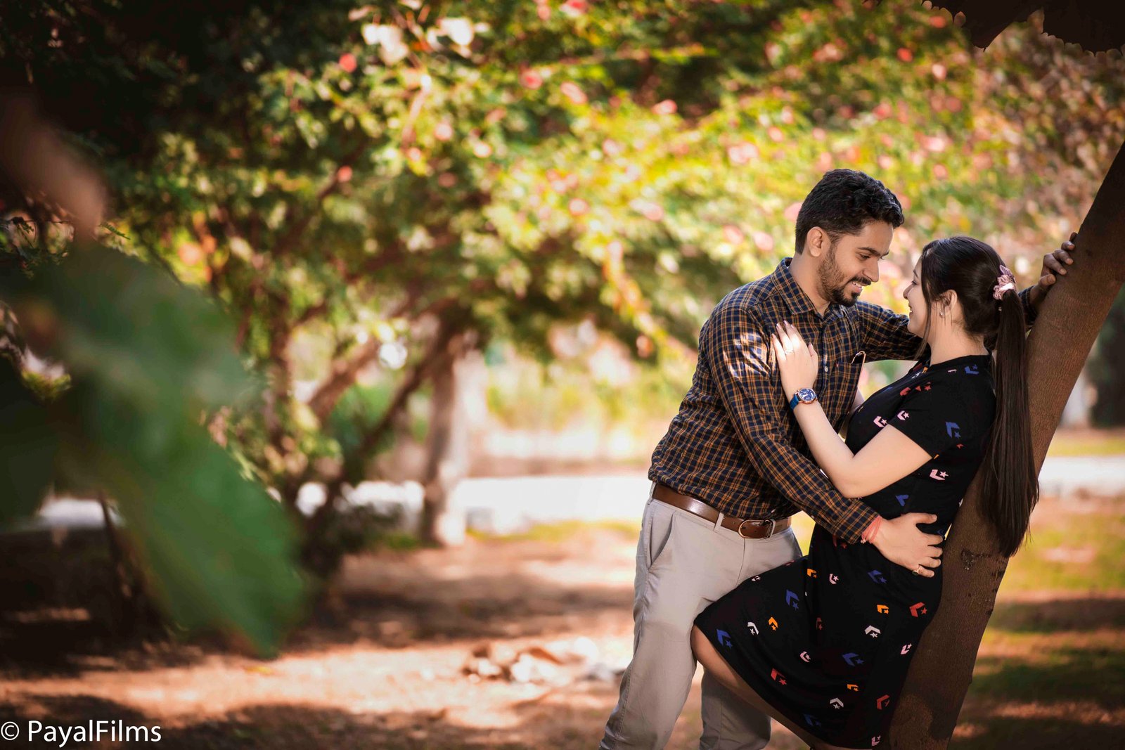 Indian couple dancing happily in traditional ethnic wear with palm trees and a historic clock tower by Payal Films.