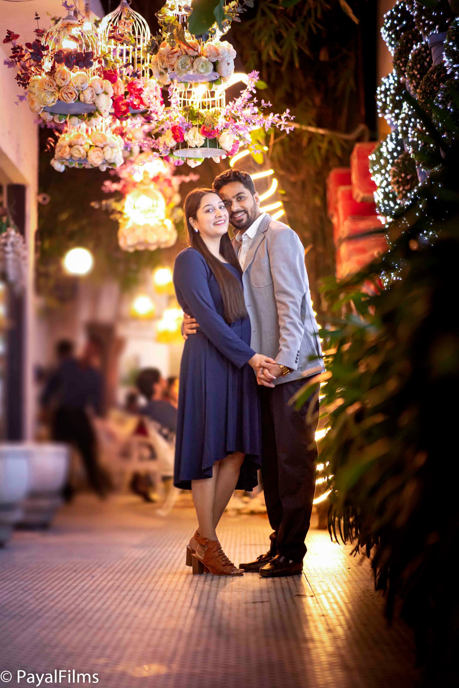 A romantic couple holding hands under floral birdcage lights, captured by Payal Films in a cinematic night portrait.
