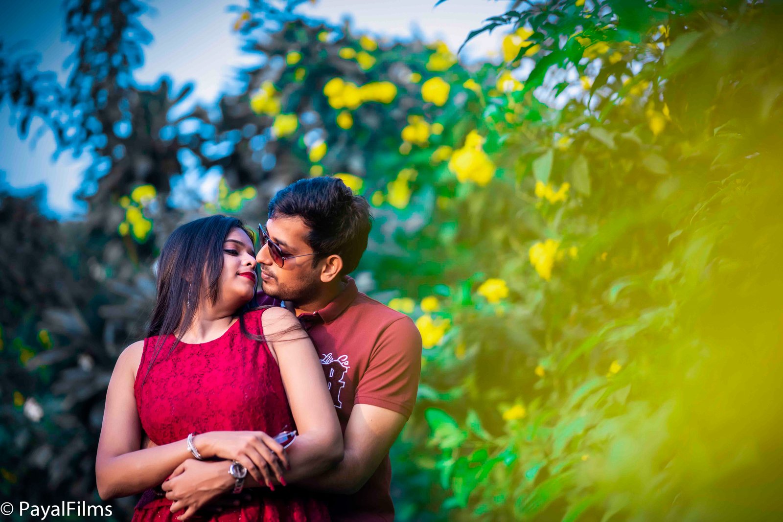 Romantic pre-wedding portrait of a couple in a red dress and brown shirt surrounded by yellow flowers by Payal Films