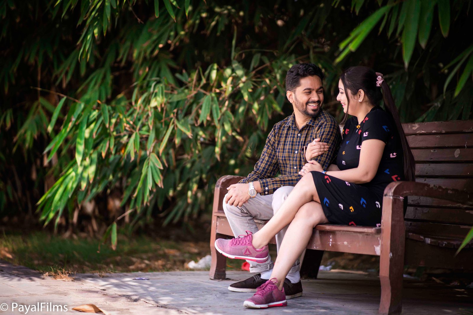 Romantic couple sitting on a park bench smiling at each other by Payal Films