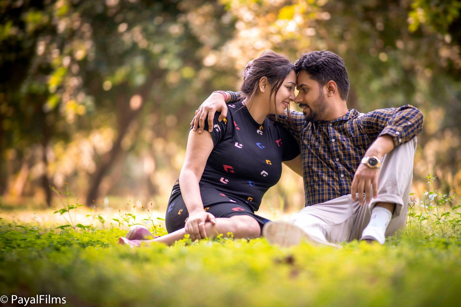 Romantic couple sitting together on lush green grass with foreheads touching, captured by Payal Films in Khagaria.