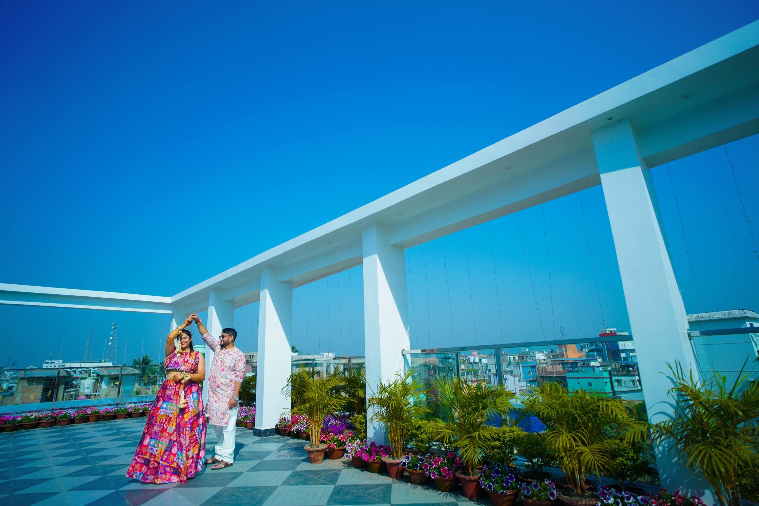 Couple dancing on rooftop terrace adorned with plants, under a clear sky and cityscape view.