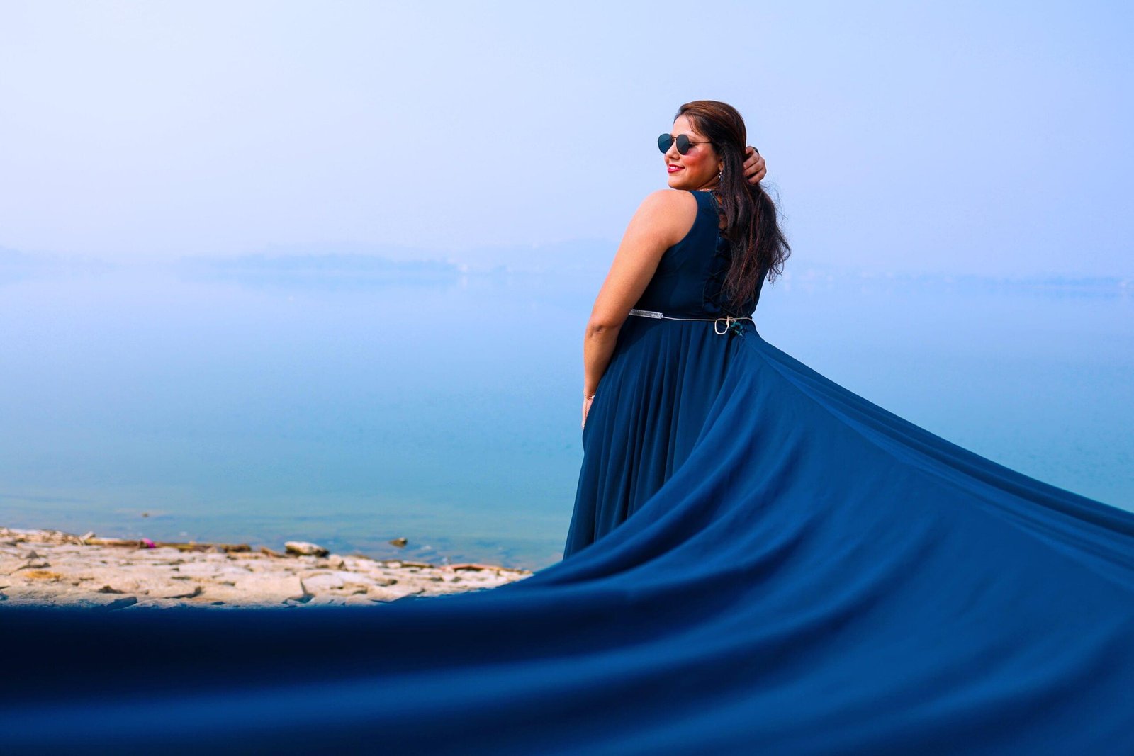 Woman in blue dress and sunglasses by calm water with flowing dress behind her - Payal Films Bihar