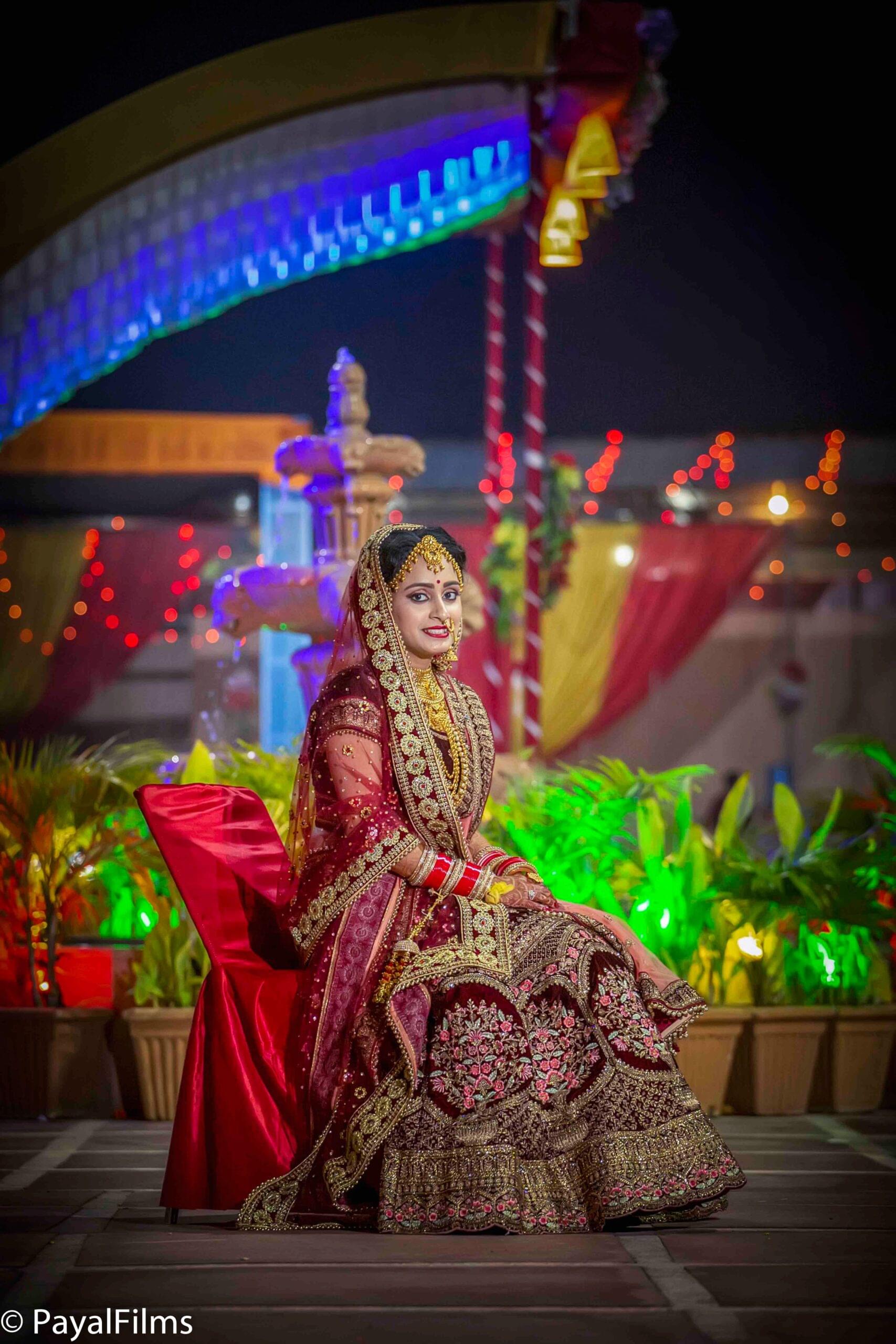 Payal Films bride in rich maroon lehenga seated outdoors during a night wedding ceremony in Khagaria