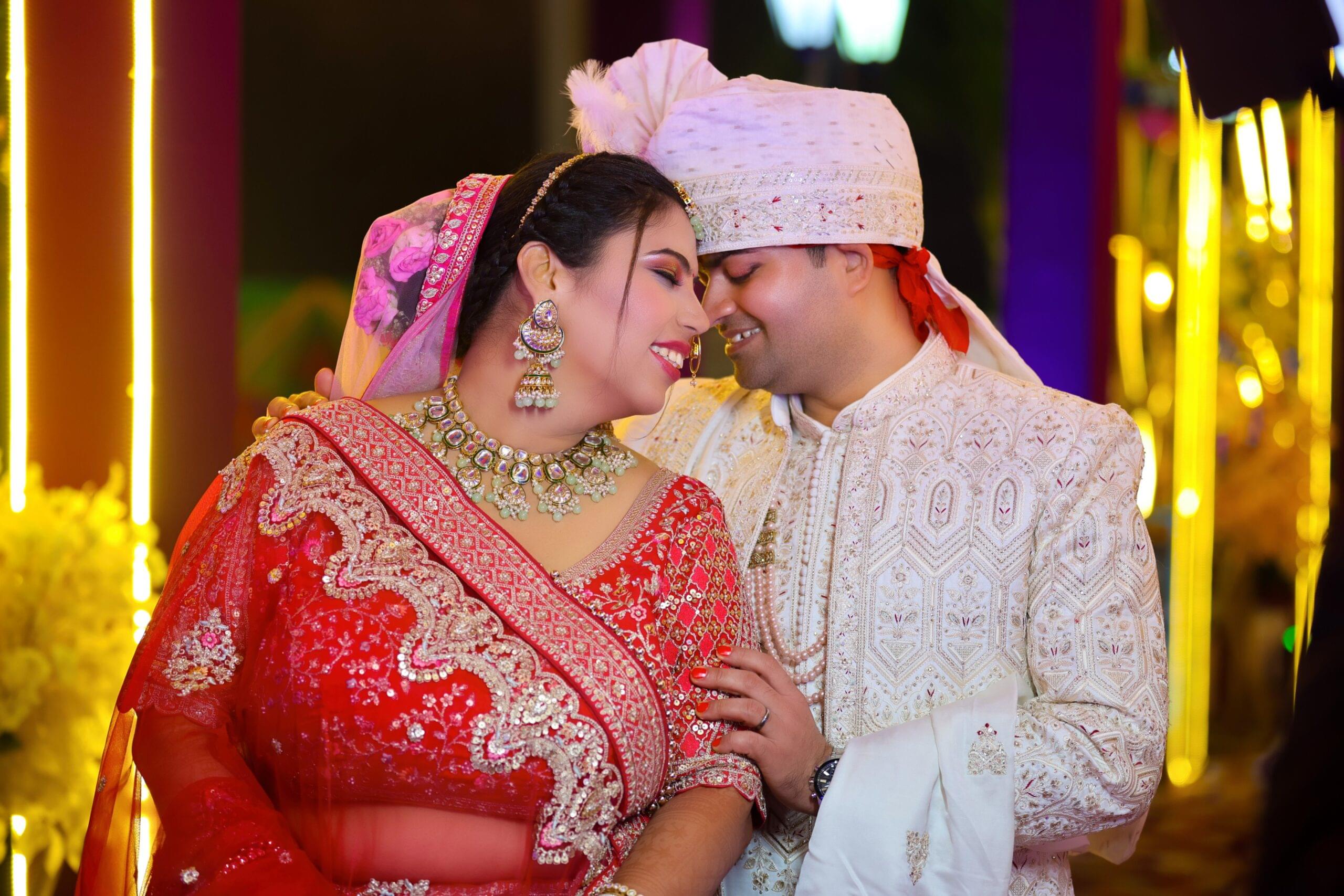 Indian bride in red embellished saree with heavy jewelry and groom in ivory embroidered sherwani and safa during wedding ceremony