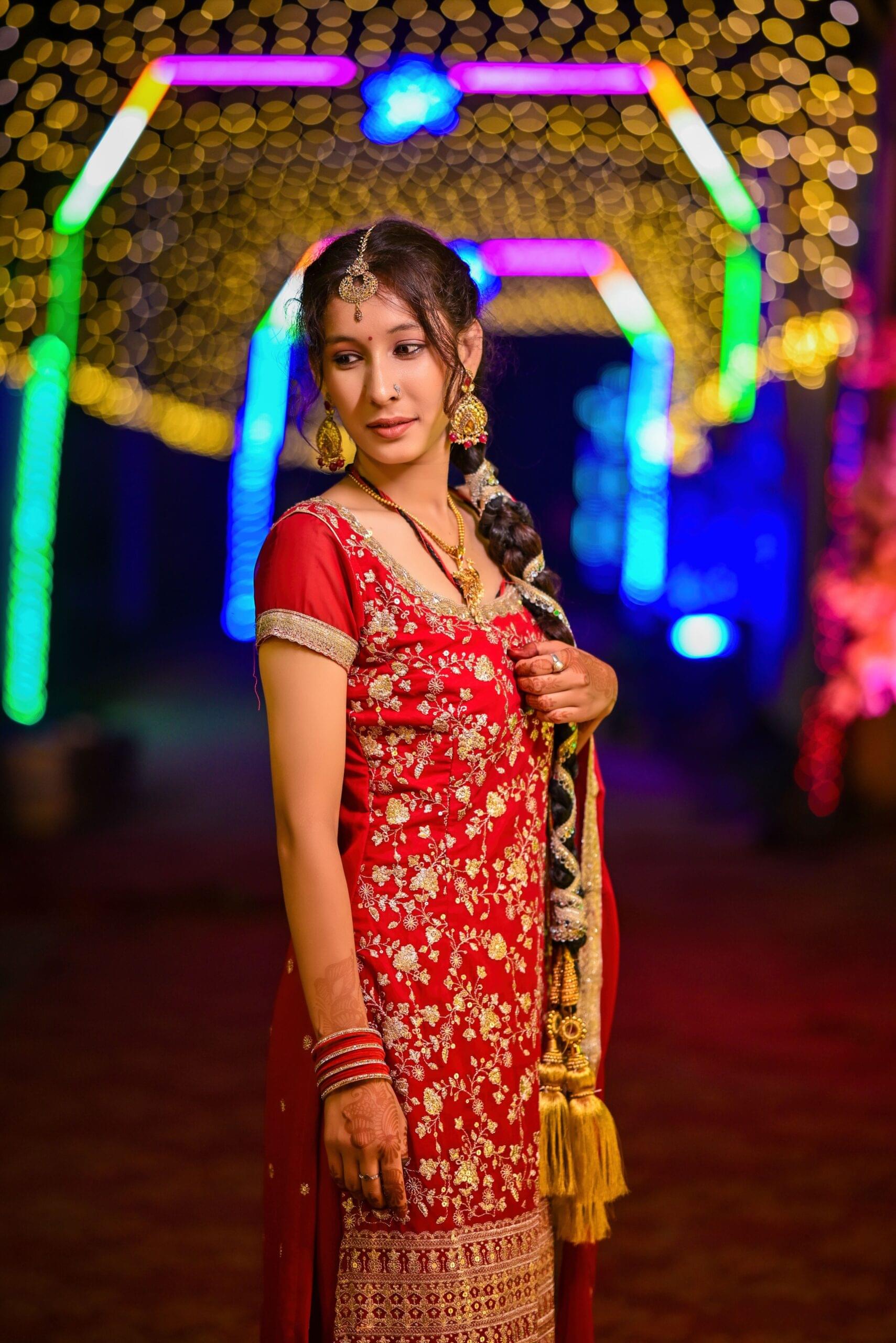 Stunning side-pose bridal portrait featuring red lehenga with golden embroidery, traditional braided hairstyle, maang tikka, and chandbali earrings by Payal Films