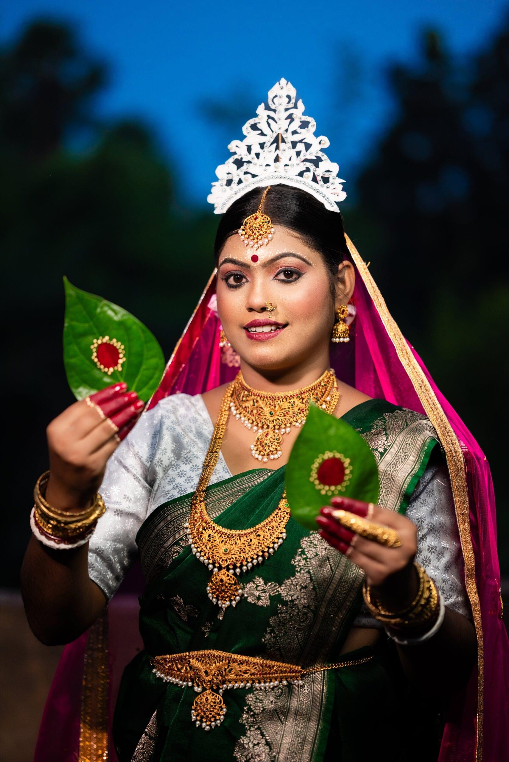 Bengali bride in traditional green saree and gold jewelry, holding decorated betel leaves (gachkouto) during wedding ceremony. Outdoor portrait, Khagaria, Bihar.
