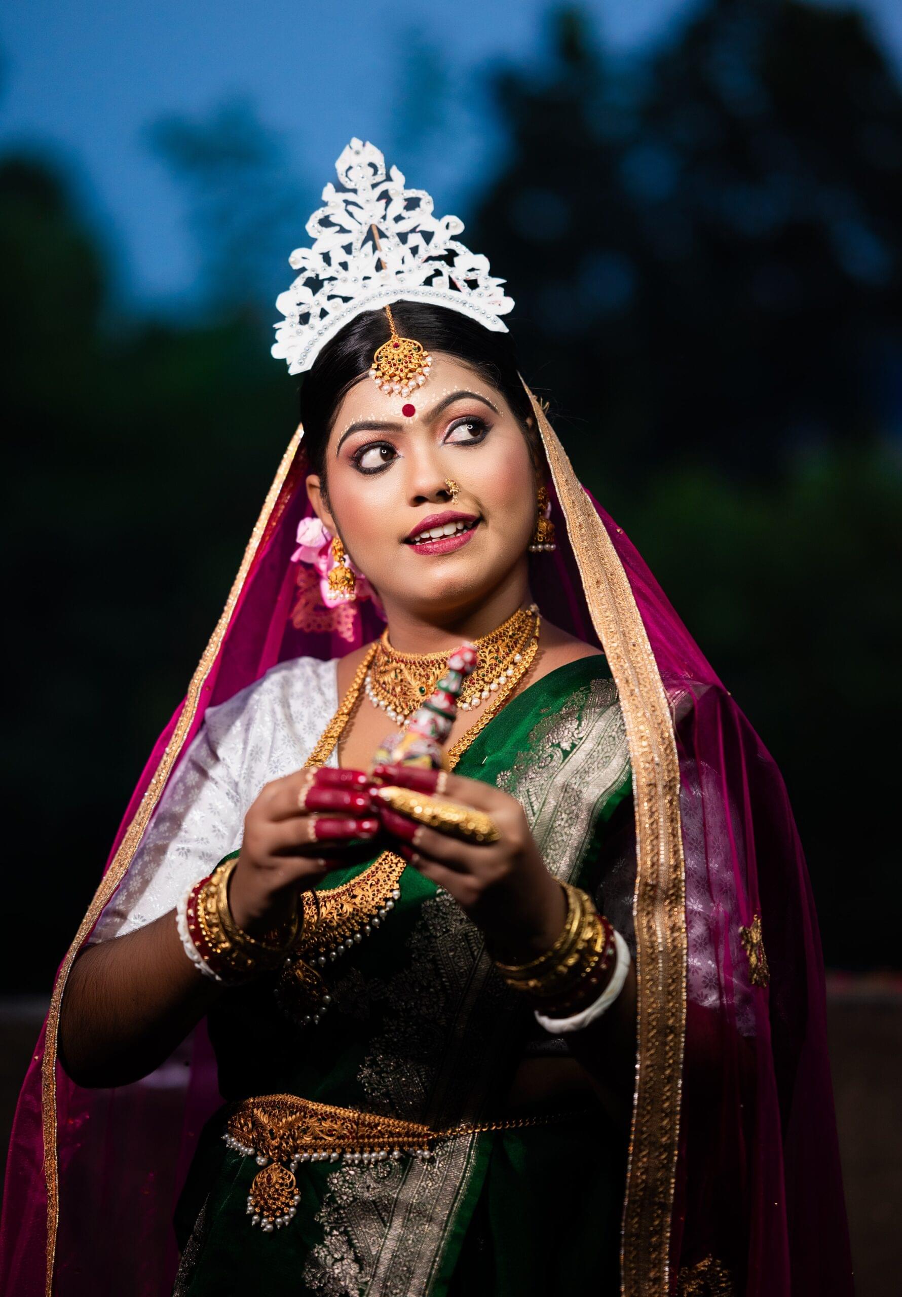 Bengali bride in a green saree and gold jewelry, holding the dirghagaur clay idol during traditional wedding rituals, Khagaria, Bihar.