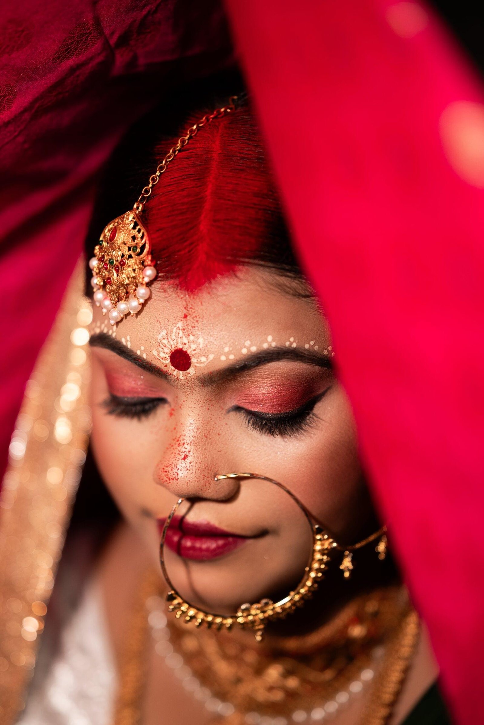 Indian bride with vibrant red sindoor and gold maang tikka, framed by a red dupatta and adorned in traditional wedding jewelry. Hindu bridal ritual, Khagaria, Bihar - Payal Films Bihar