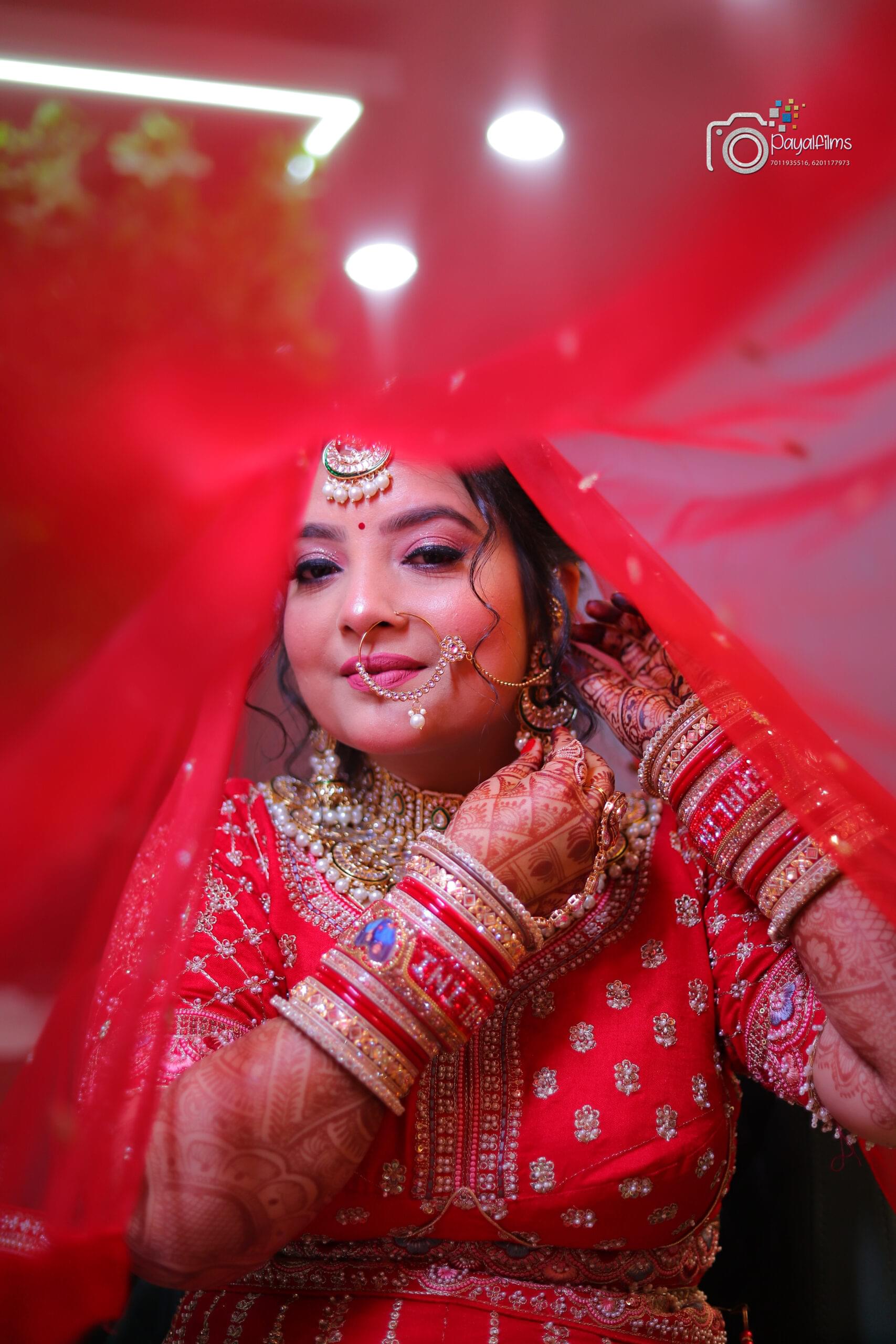 Indian bride in red lehenga adjusting earrings under dupatta, detailed mehndi and chooda – Payal Films wedding photography Khagaria Bihar